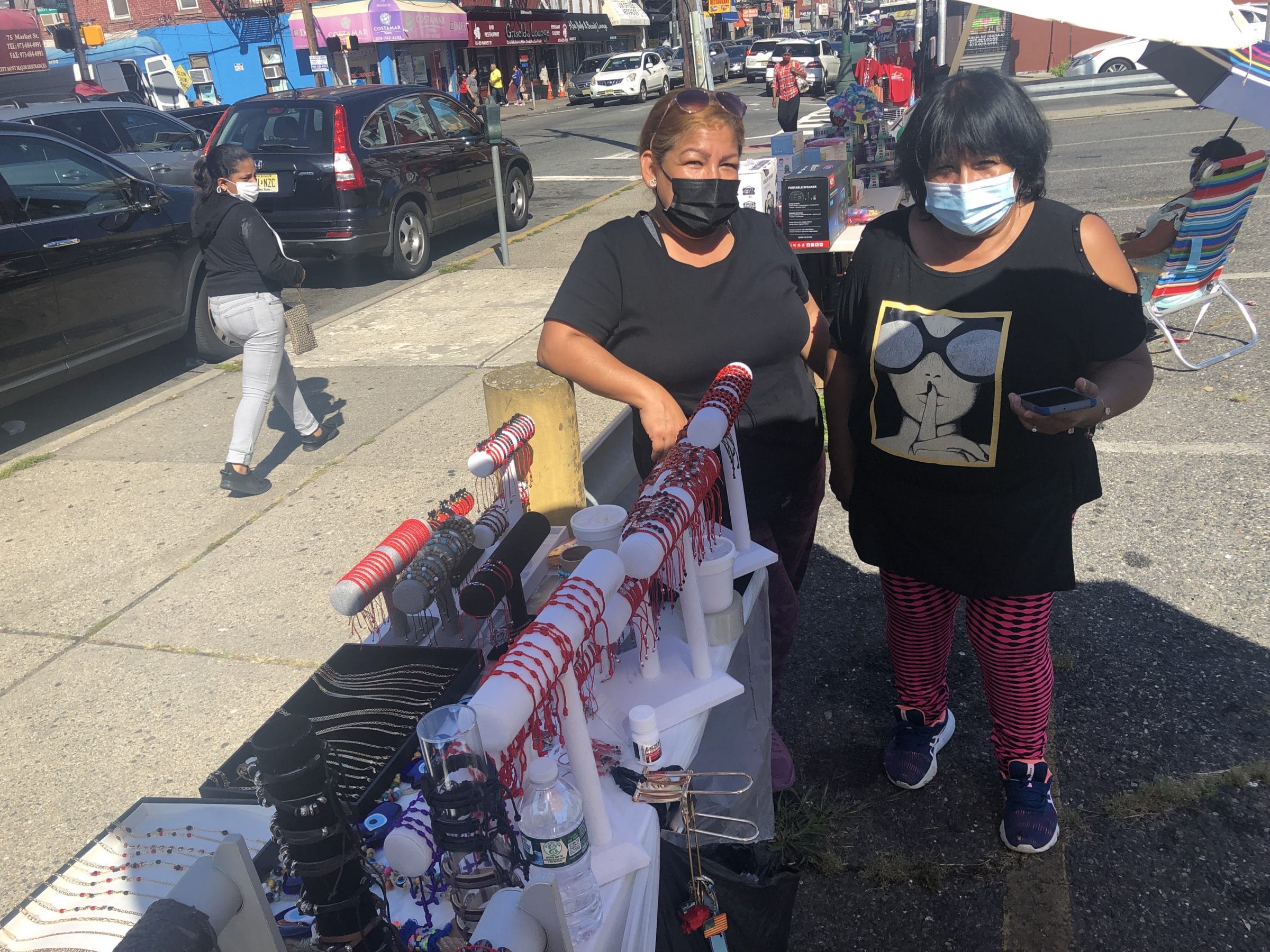 Two Latina women stand in front of a street vendor cart in Paterson, NJ where they sell Peruvian sport shirts.