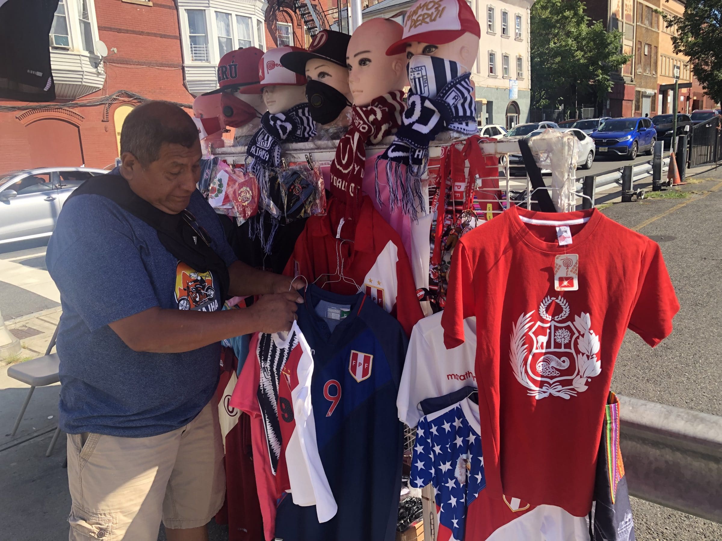 A Latino man hangs up articles of clothing on a street vendor cart he owns.