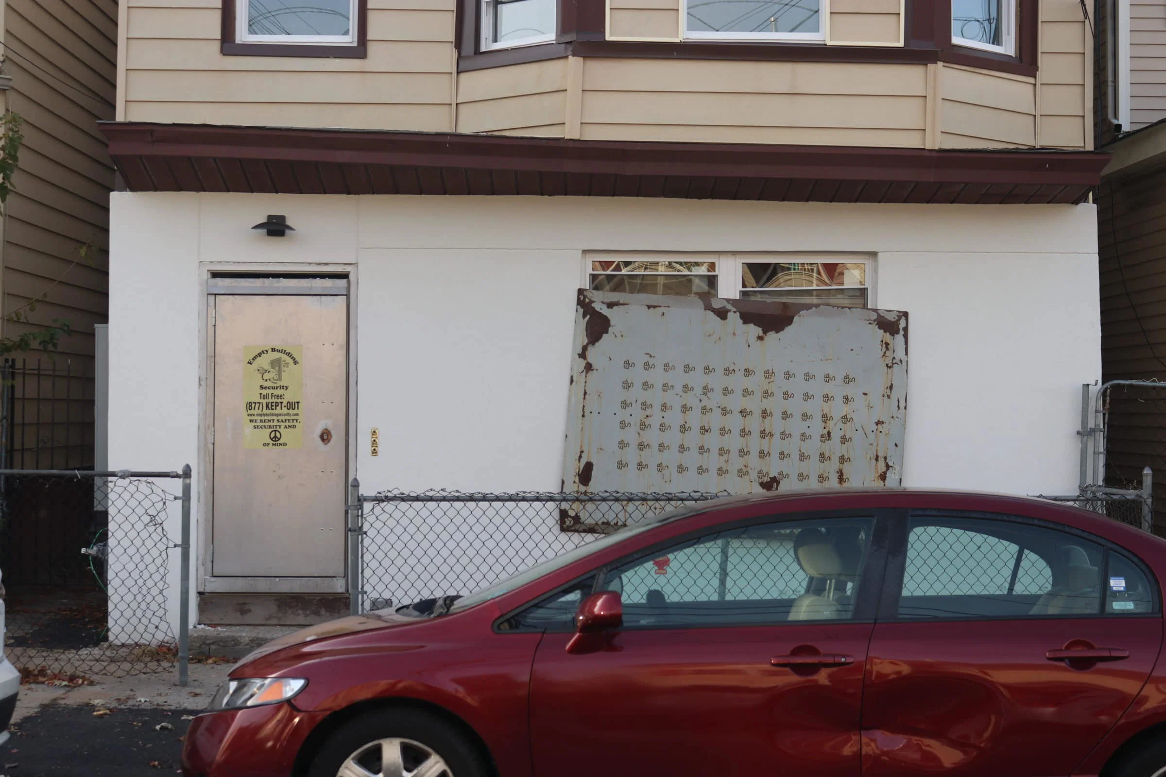 A red car is parked in front of a foreclosed home in Paterson, NJ.